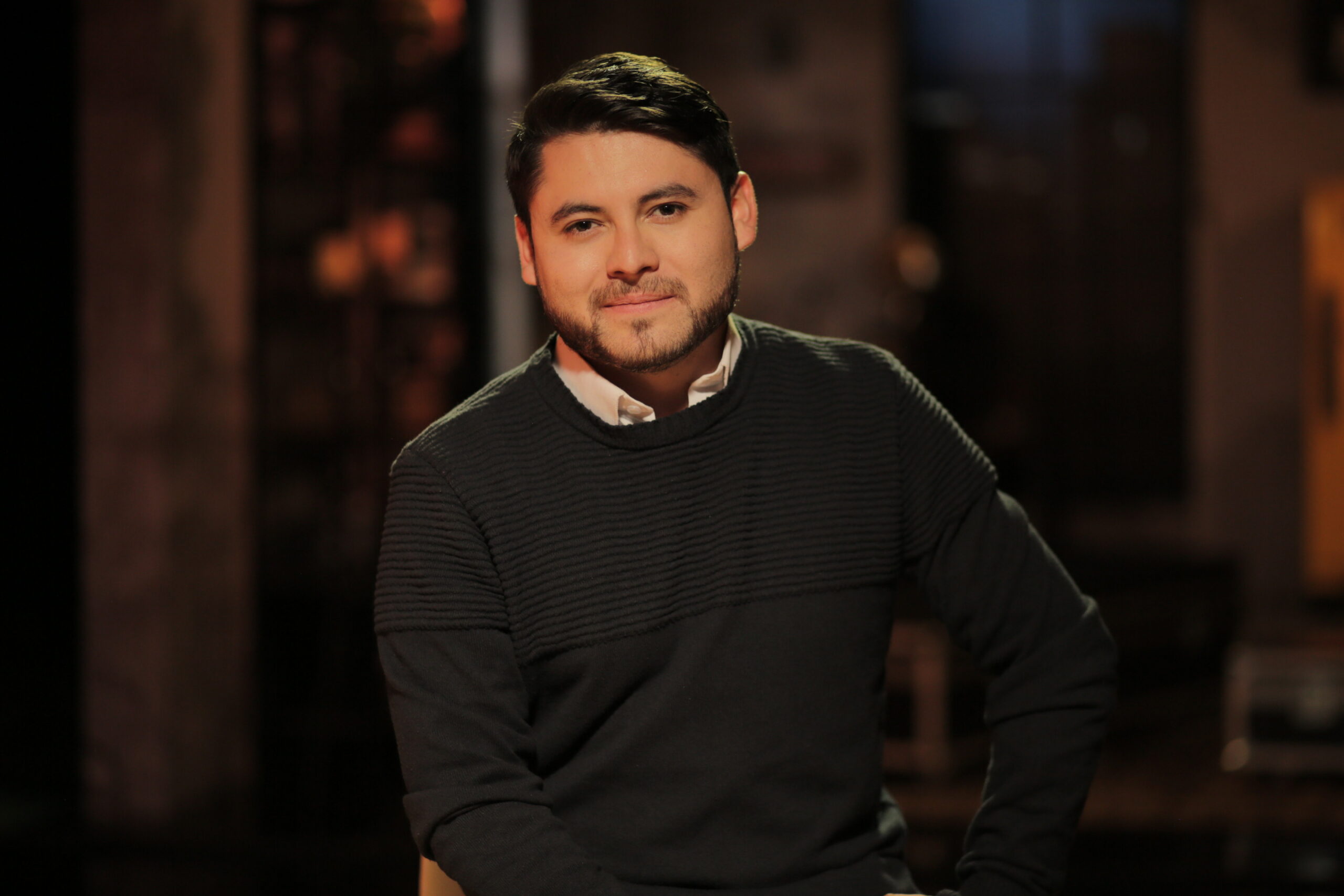 Cristian León, periodista de AHORA, vestido de saco negro y camisa blanca, con una mano sobre la cadera.