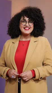 Jenny Bastidas, periodista cultural de AHORA, vestida de blazer beige y camisa roja, sonriendo en el set de AHORA.