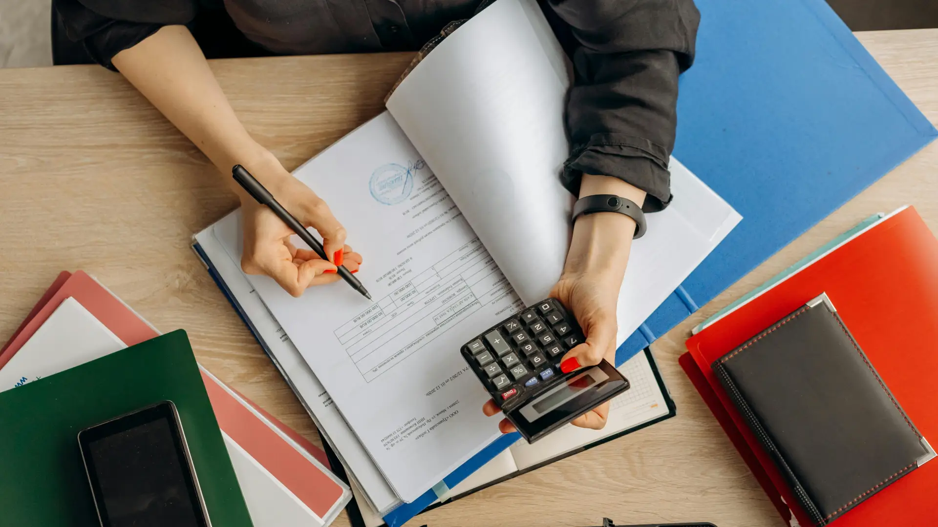 Imagen de puesto de trabajo donde hay unas manos, una tiene una calculadora y la otra un lapicero