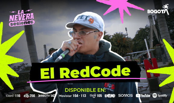 Cantante de El RedCode con gorra y gafas interpreta con micrófono en mano durante presentación en vivo al aire libre, con otras personas y entorno urbano al fondo en Bogotá