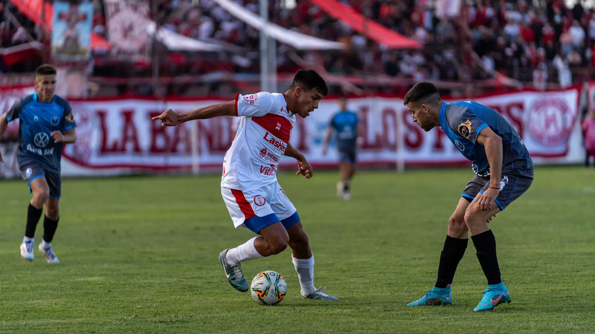 Futbolista con balon enfrentando a otro en medio de un campo de futbol en un estadio