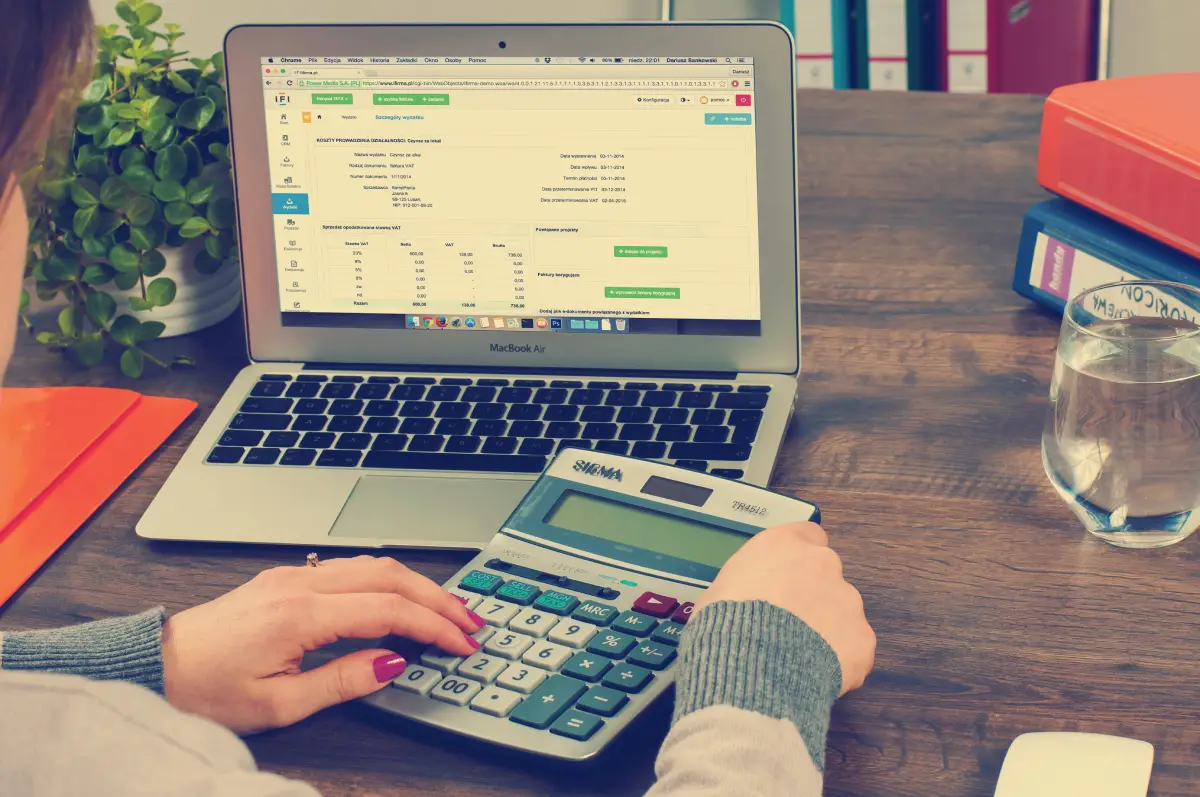 Una mujer hace cuentas en una calculadora revisando su computador
