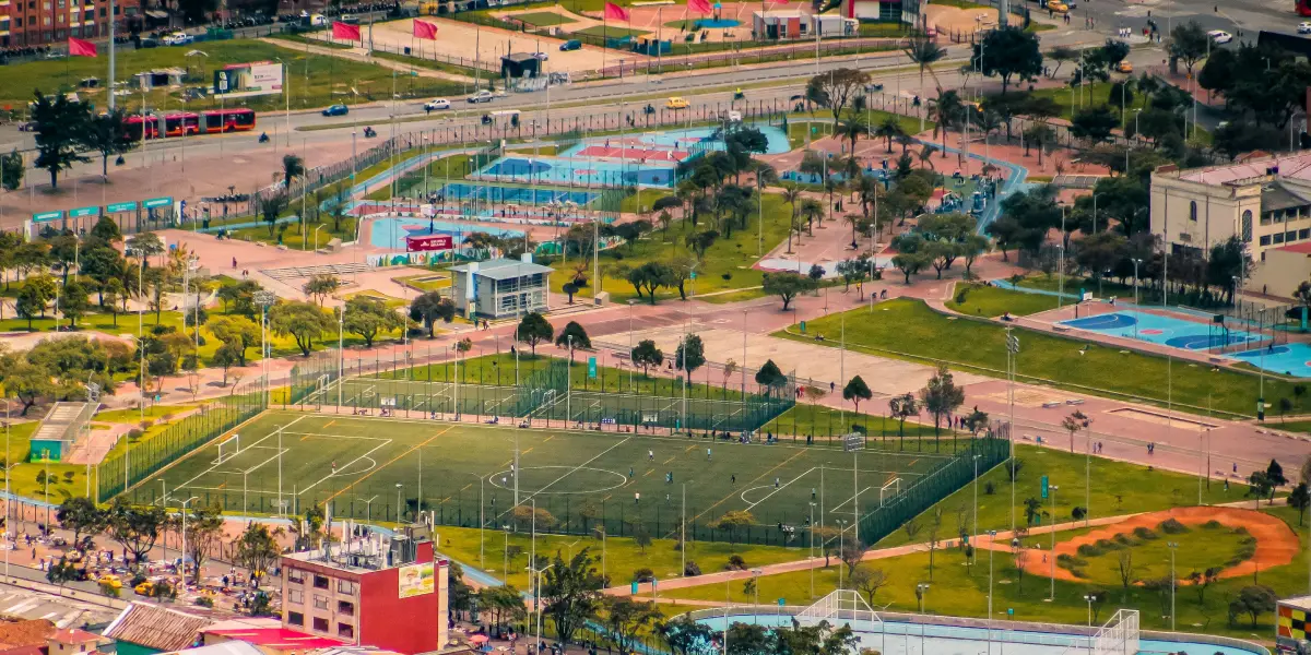 Una vibrante imagen aérea de un complejo deportivo con campos de fútbol y parques llenos de actividad.