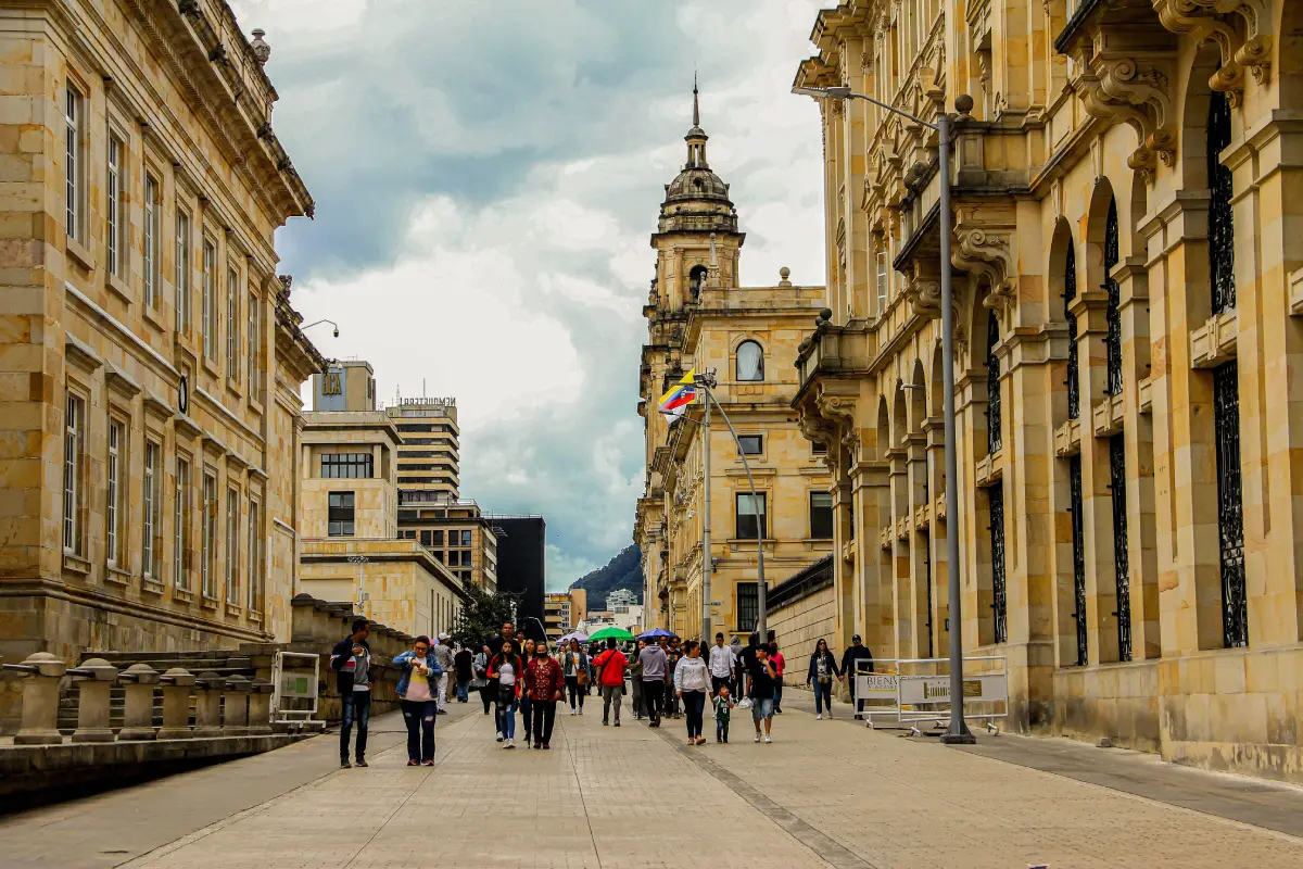 Gente caminando en Bogotá con edificios históricos y la bandera colombiana a la vista.