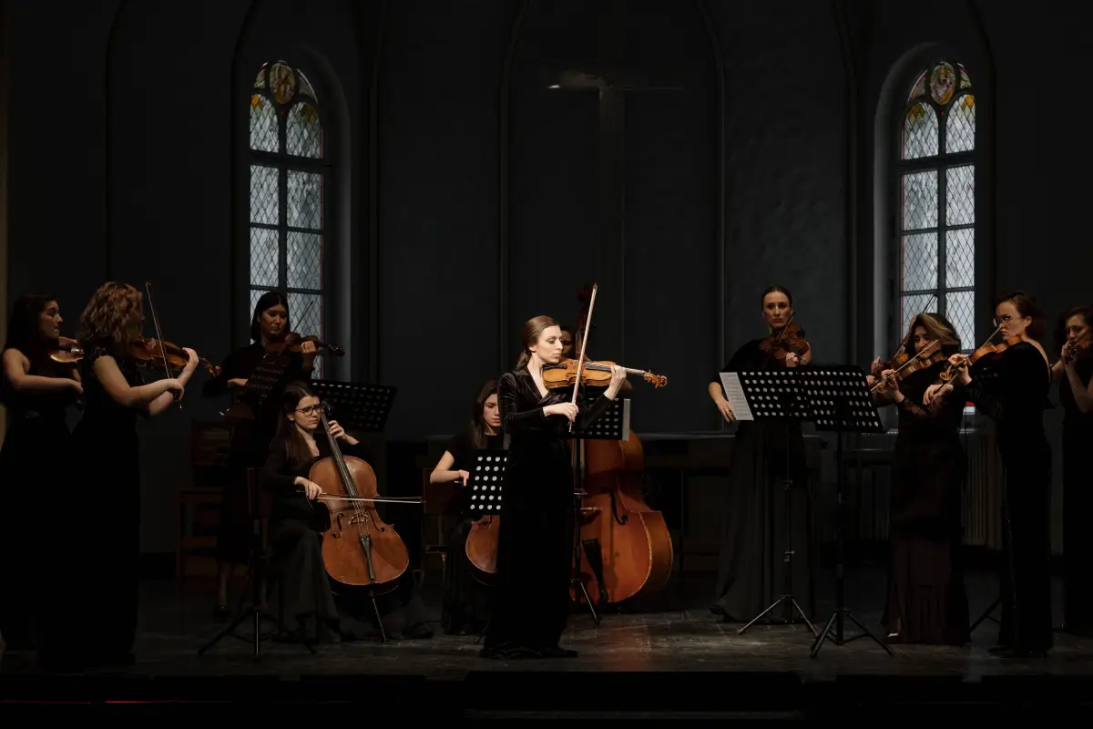 Músicas mujeres interpretan con violines y cellos en un entorno de orquesta clásica.