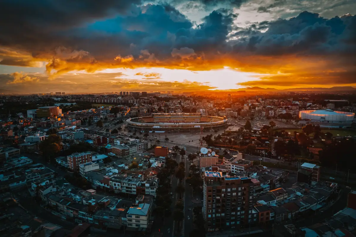 Una impresionante vista aérea de Bogotá al atardecer mostrando el vibrante paisaje urbano y las nubes dramáticas.