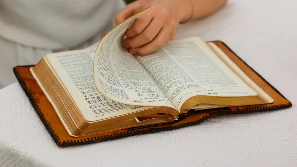 La mano de una persona pasando las páginas de una Biblia abierta, creando una escena de estudio tranquila.