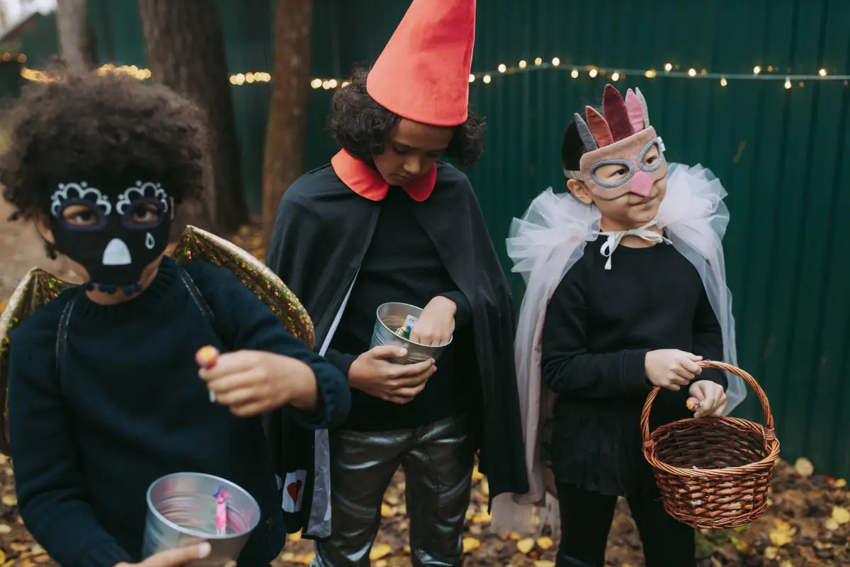 Tres niños con disfraces creativos de Halloween recolectan caramelos al aire libre.